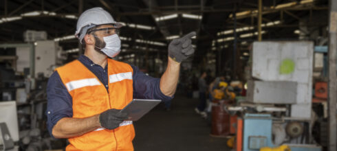 safety director in ppe mask and using clipboard to direct employees in industrial facility
