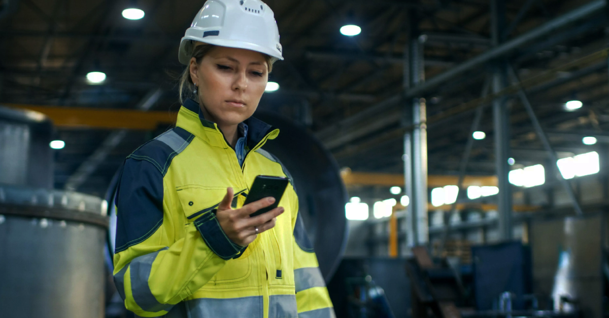 female safety worker in hi-vis ppe and hard hat looking at mobile phone