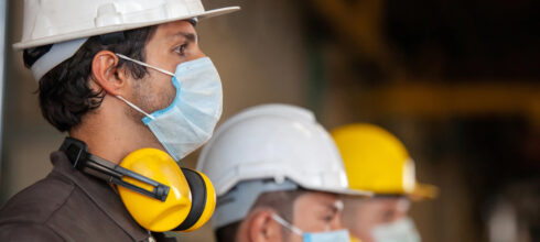 Safety employees in hard hats and COVID masks wearing ear protection around their neck