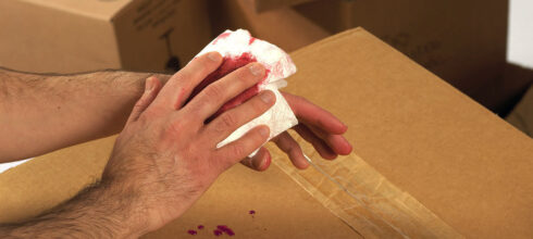 employee's hand bleeding above box in industrial storeroom
