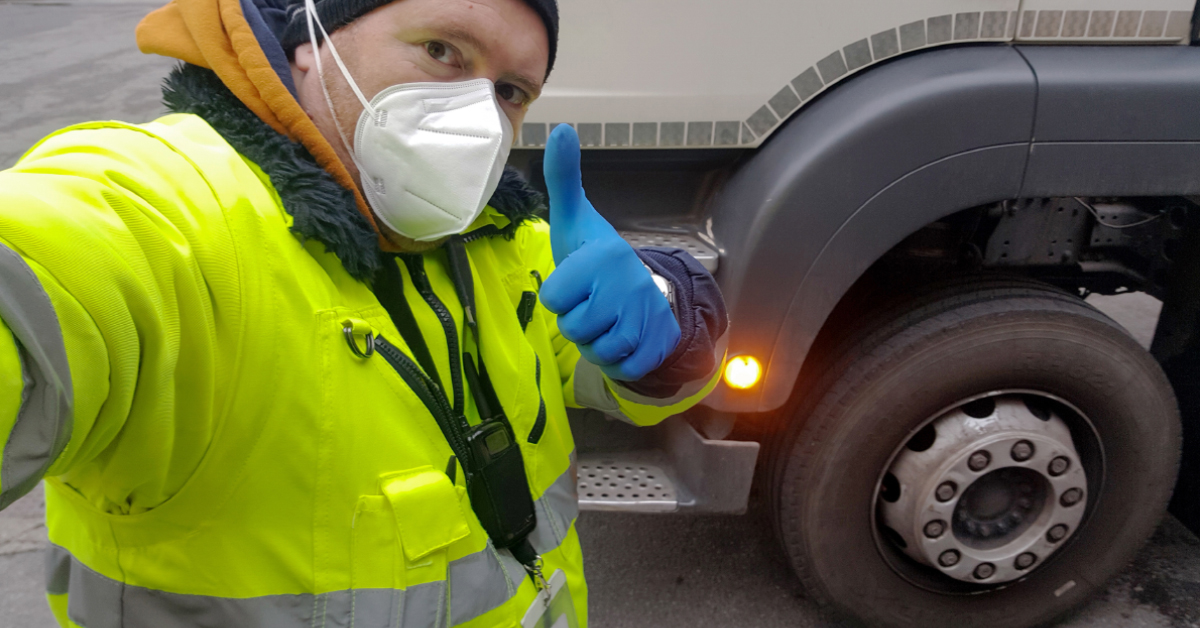 Driver employee wearing safety mask and hi-vis vest giving thumbs up in front of commerical vehicle