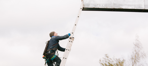 Billboard installer climbing ladder at height