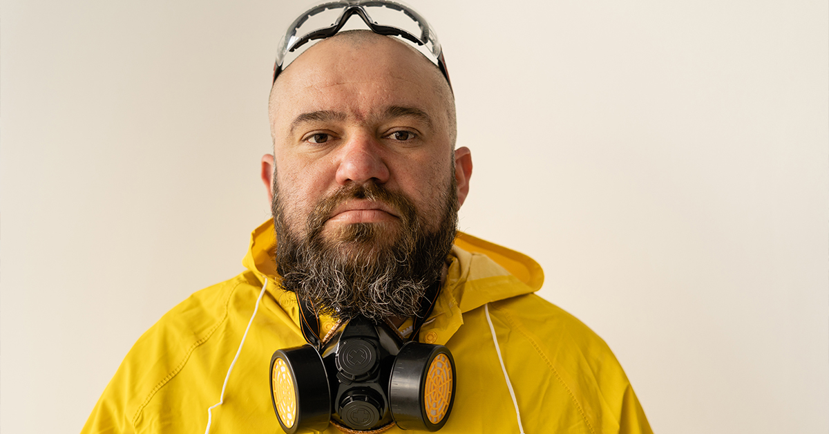 Man with beard wearing a respirator, safety glasses and yellow hazmat suit