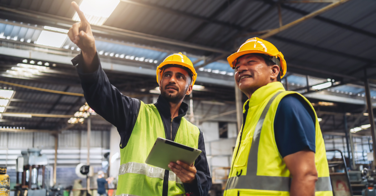Safety worker pointing in warehouse with an ipad in hand to another safety worker