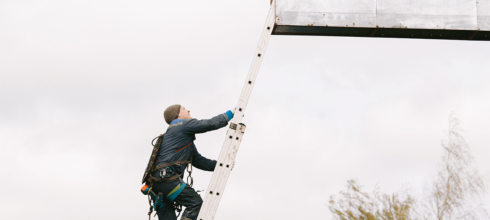 Billboard installer climbing ladder at height