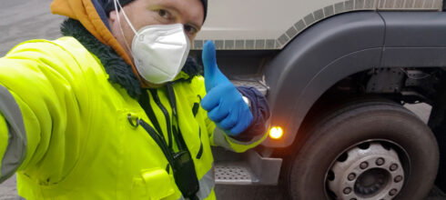 Driver employee wearing safety mask and hi-vis vest giving thumbs up in front of commerical vehicle