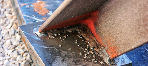 Close-up image of a welded metal joint with visible welding spatter and slight corrosion on the surface, illustrating issues in the welding process.