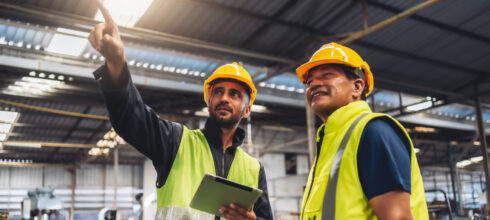 Safety worker pointing in warehouse with an ipad in hand to another safety worker