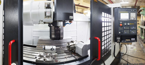 A close-up view of a CNC machine inside an industrial shop, showing the control panel, workspace, and cutting tool setup.