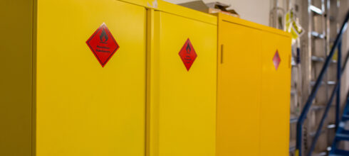 A row of bright yellow flammable storage cabinets with hazard warning labels, designed to safely store hazardous substances.