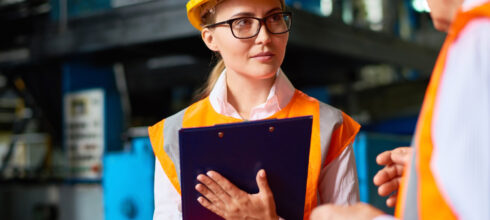 woman in safety hat and vest holding clipboard