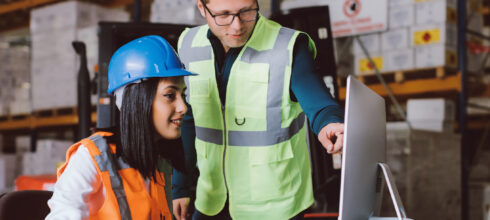 industrial employee in safety ppe showing another employee something on the computer