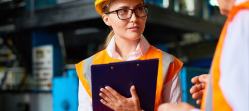 woman in safety hat and vest holding clipboard